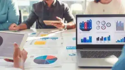 Team analyzing data charts on laptop and tablet in a bright office setting, focusing on business growth and strategy insights.