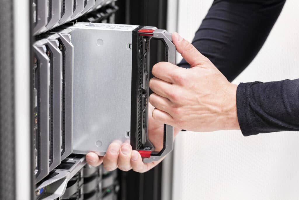 Hands inserting a server drive into a data center rack, highlighting IT hardware management and data storage solutions.