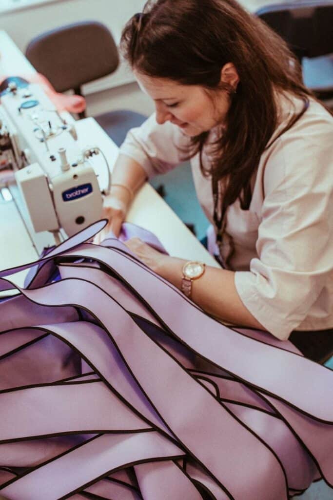Woman sewing purple fabric with a machine in a design studio. Craftsmanship and creativity in textile design.