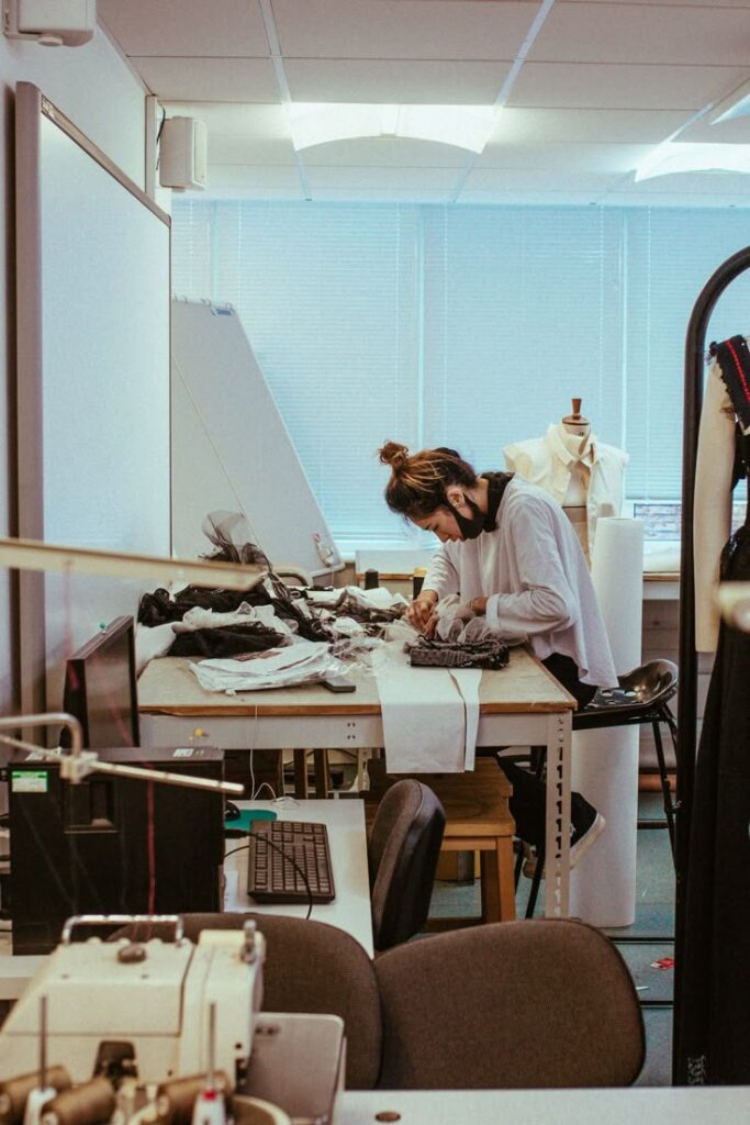 Fashion designer working on garment creation in a design studio, surrounded by sewing equipment and fabric materials.