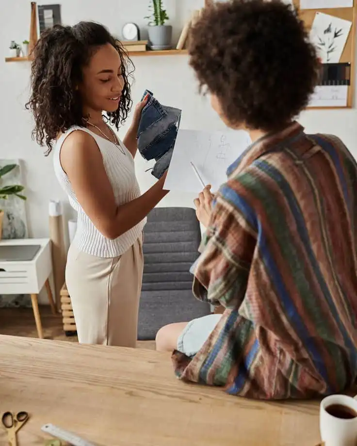 Dont Wait to Ask for Help Two women collaborate on fashion design, discussing fabric swatches and sketches in a creative workspace. | Sky Rye Design Two women collaborate on fashion design, discussing fabric swatches and sketches in a creative workspace.