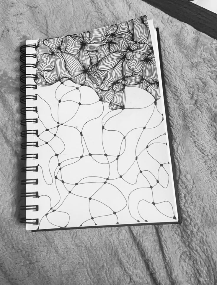 Black and white abstract line drawing in a spiral notebook on a soft, textured surface.