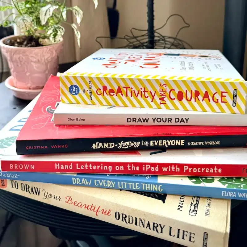 Drawing-Books-I-love Stack of art and lettering books on a table, including titles on creativity, drawing, and hand lettering techniques, next to a potted plant. | Sky Rye Design Stack of art and lettering books on a table, including titles on creativity, drawing, and hand lettering techniques, next to a potted plant.
