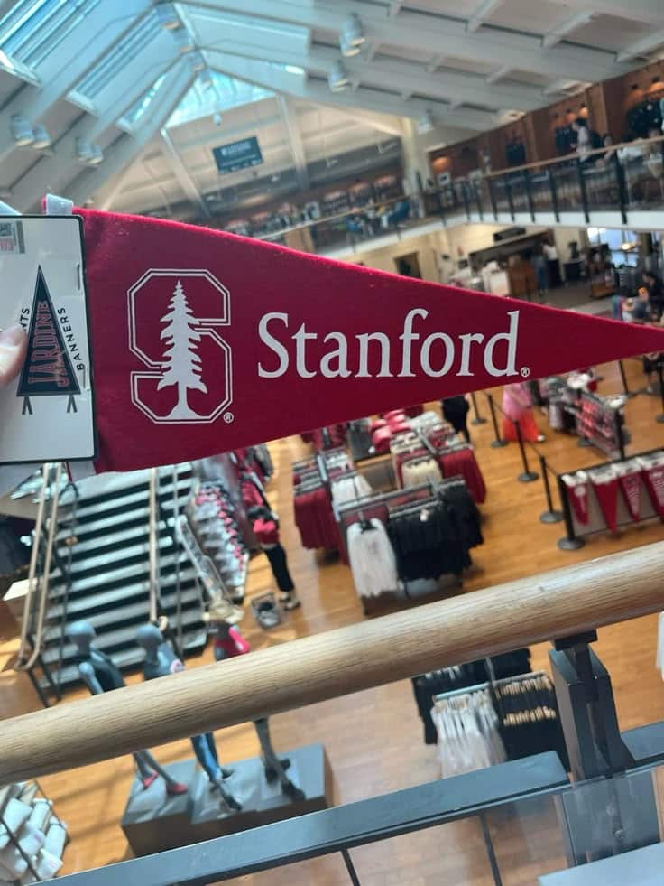 Dream 😍 Red Stanford pennant displayed inside a university store, featuring clothes and gear, under a skylit roof. | Sky Rye Design Red Stanford pennant displayed inside a university store, featuring clothes and gear, under a skylit roof.
