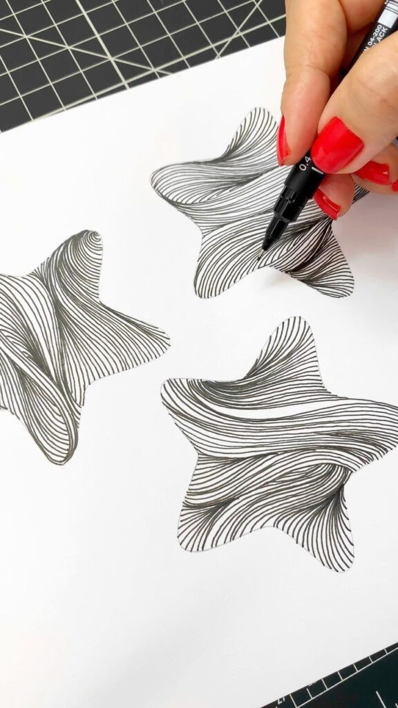 Hand drawing intricate star shapes with black pen on white paper, creating a mesmerizing geometric pattern.