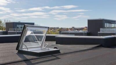 Skylight window open on a flat rooftop against a clear blue sky, showcasing modern architecture and urban skyline in the background.