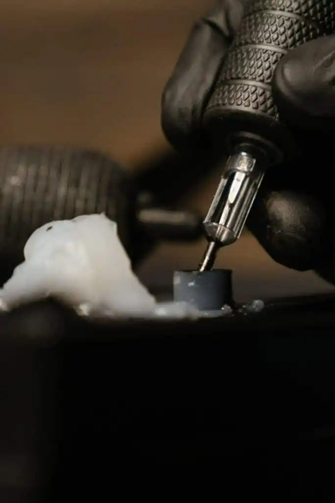 Close-up of a tattoo machine needle with a black glove, showcasing precision and detail in tattoo artistry.