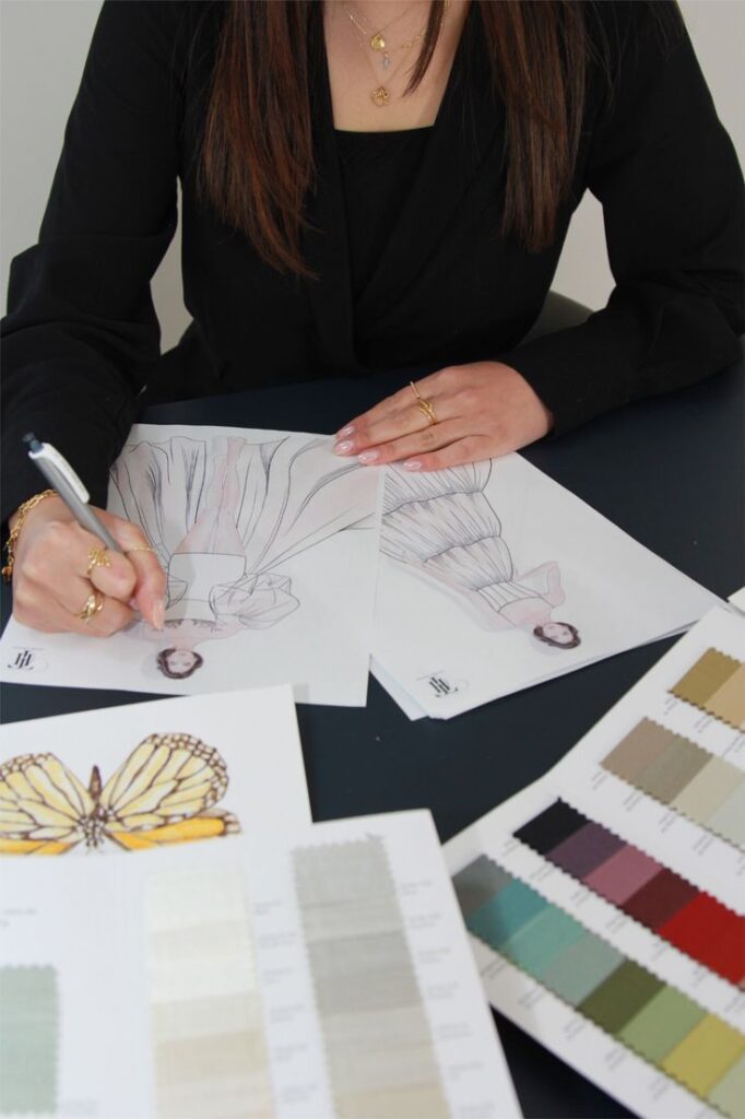 Fashion designer sketching dress ideas with color swatches and butterfly inspiration on table. Creativity in fashion design workspace.