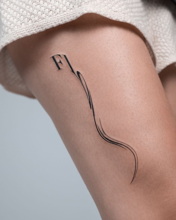 Minimalist thigh tattoo with elegant flowing design and black ink detailing.