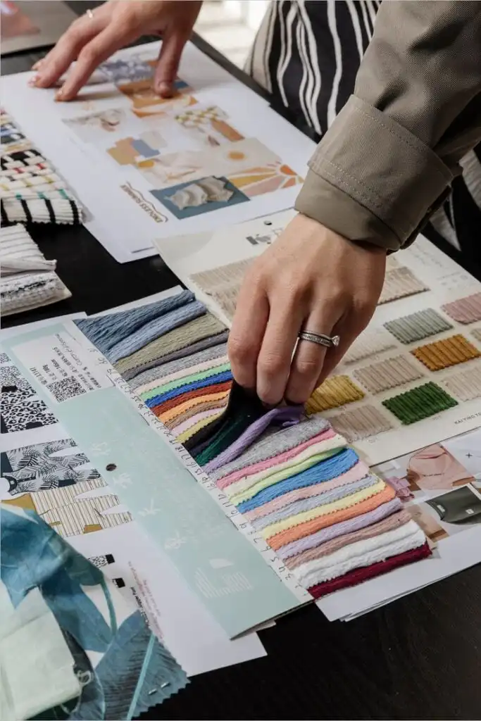 Fashion Fabric Swatches Designer selecting colorful fabric swatches and reading pattern catalogs for interior design project on a desk. | Sky Rye Design Designer selecting colorful fabric swatches and reading pattern catalogs for interior design project on a desk.