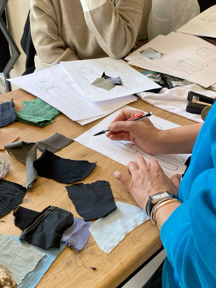 Fashion designers sketching outfits on paper surrounded by colorful fabric swatches for design inspiration.