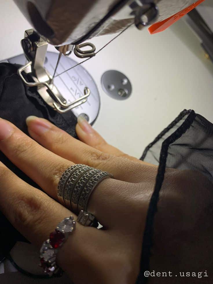 Fashion designer sewing aesthetic by me dent_usagi 1 Close-up of a hand sewing black fabric on a machine, adorned with silver and gemstone rings, symbolizing craft and elegance. | Sky Rye Design Close-up of a hand sewing black fabric on a machine, adorned with silver and gemstone rings, symbolizing craft and elegance.