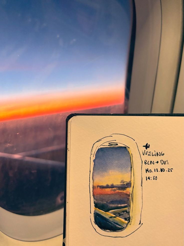 Airplane window view of a vibrant sunset with a sketch of the scene in a notebook, illustrating travel inspiration and creativity.