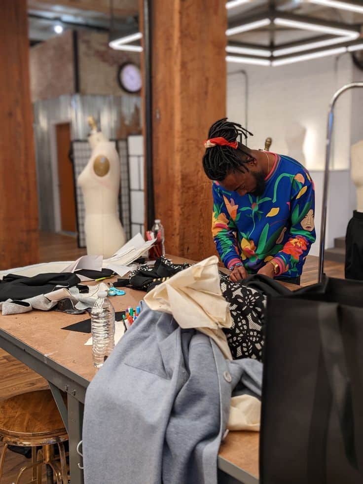 Designer working on fashion pieces at a sewing studio with colorful thread and fabric, surrounded by mannequins and sewing tools.