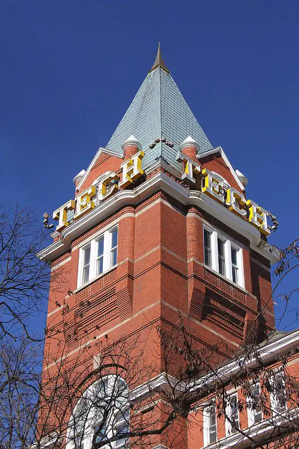 Historic brick tower under clear blue sky with TECH signage, surrounded by winter trees, showcasing classic architectural details.