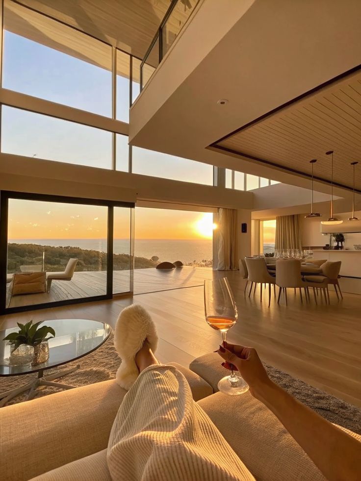 Golden Hour Serenity ✨ _ Modern Luxury Living Enjoying a sunset view from a luxurious living room with a glass of wine, fuzzy slippers, and modern decor. Relaxation and elegance combined. | Sky Rye Design Enjoying a sunset view from a luxurious living room with a glass of wine, fuzzy slippers, and modern decor. Relaxation and elegance combined.