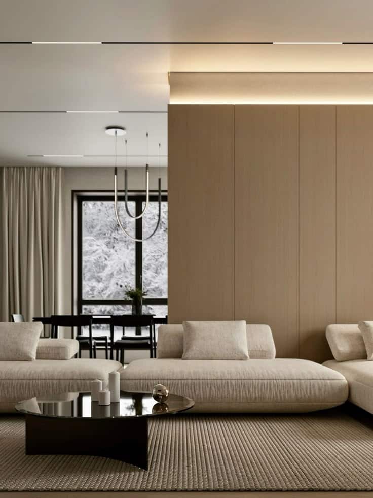 Modern living room with beige sofas, a round coffee table, and a large window overlooking a snowy landscape. Contemporary interior design.