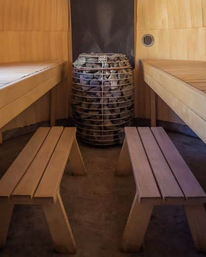 Wooden sauna interior with benches, centered stone heater, and warm lighting, creating a relaxing and tranquil atmosphere.