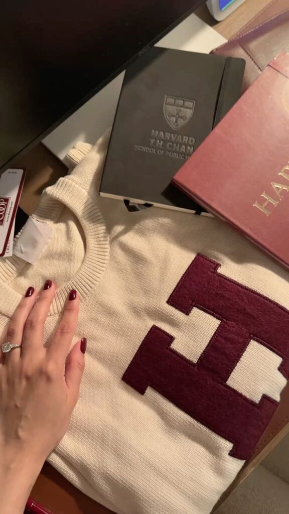 Harvard summer orientation Hand on a sweater with an 'H', alongside Harvard books on a desk. Educational gear and study materials arrangement. | Sky Rye Design Hand on a sweater with an 'H', alongside Harvard books on a desk. Educational gear and study materials arrangement.