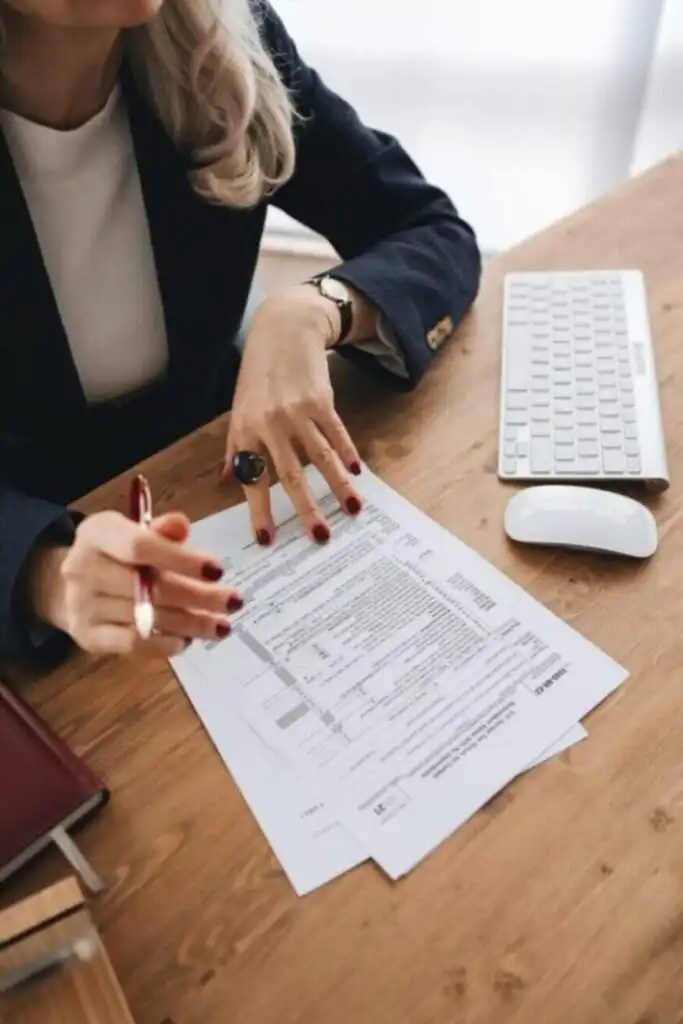 Businesswoman reviewing documents at desk with keyboard, mouse, and planner in office setting.