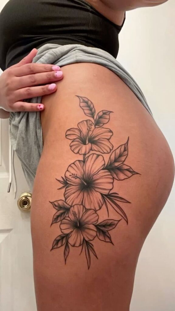 Hibiscus flower patch tattoo 🌺 Detailed floral tattoo on thigh featuring hibiscus flowers and leaves, showcasing intricate black and gray ink design. | Sky Rye Design Detailed floral tattoo on thigh featuring hibiscus flowers and leaves, showcasing intricate black and gray ink design.