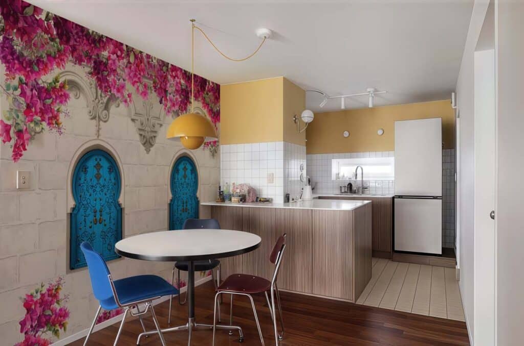 Hidden-Paradise-Floral-Escape-Wallpaper-Mural-M Colorful modern kitchen with decorative flower mural, yellow accents, round table, blue chairs, and integrated white appliances. | Sky Rye Design Colorful modern kitchen with decorative flower mural, yellow accents, round table, blue chairs, and integrated white appliances.