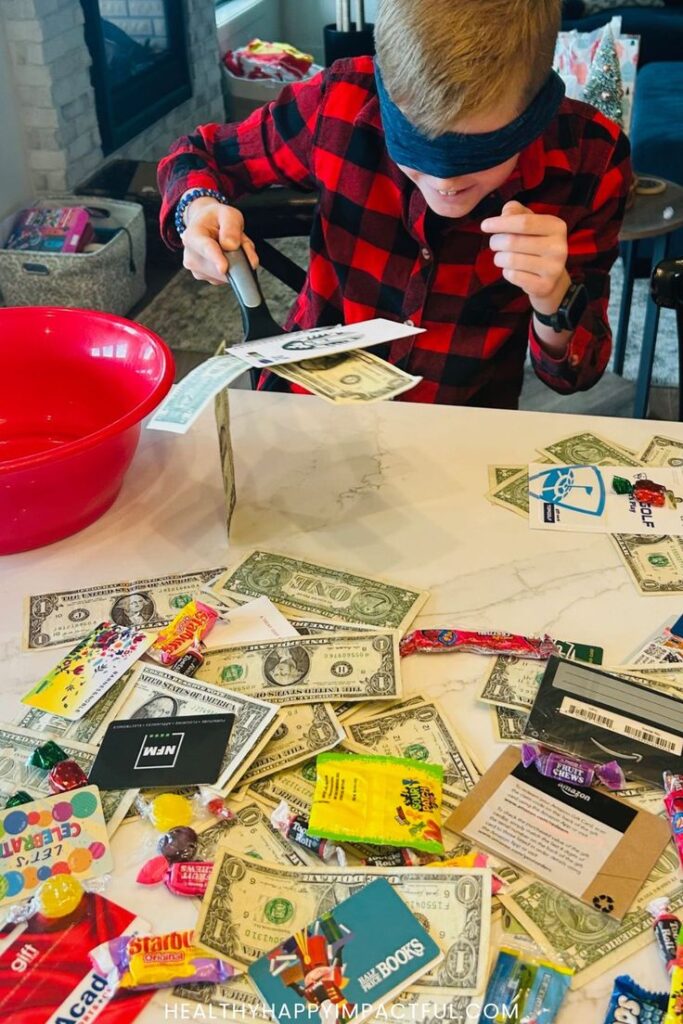 Blindfolded boy cutting paper money at table with candies and gift cards, creating a fun and engaging indoor challenge.
