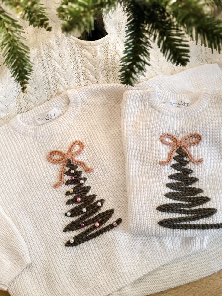 Holiday Hand Embroidered Sweater Christmas Tree Embroidered Sweater Personalized Holiday Sweater Embroidered Name Sweater Embroidery White sweaters with Christmas tree embroidery, decorated with bows and beads, under a festive pine branch. | Sky Rye Design White sweaters with Christmas tree embroidery, decorated with bows and beads, under a festive pine branch.