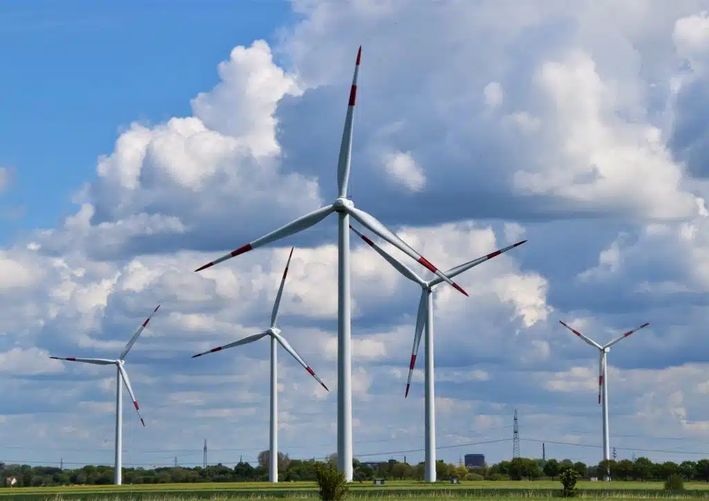 Wind turbines in a green field under a cloudy blue sky, generating renewable energy and promoting sustainable power solutions.