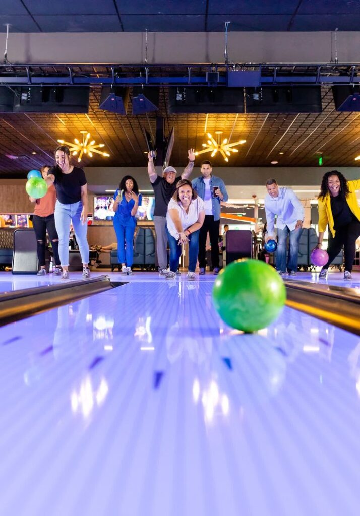 Hospitality Travel - Monika Normand Photography Group of friends enjoying a lively game of bowling under modern lights, with focus on a rolling green ball on the lane. | Sky Rye Design Group of friends enjoying a lively game of bowling under modern lights, with focus on a rolling green ball on the lane.