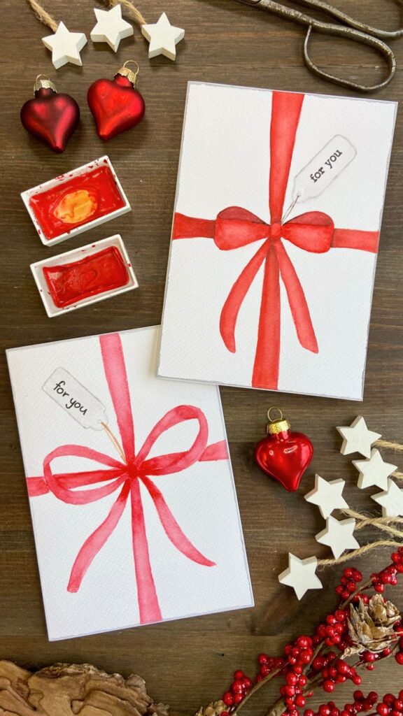 How To Paint A Watercolour Bow For Christmas Cards Handmade Christmas cards with red ribbons, ornaments, and star decorations on a wooden table. Festive holiday DIY crafting. | Sky Rye Design Handmade Christmas cards with red ribbons, ornaments, and star decorations on a wooden table. Festive holiday DIY crafting.