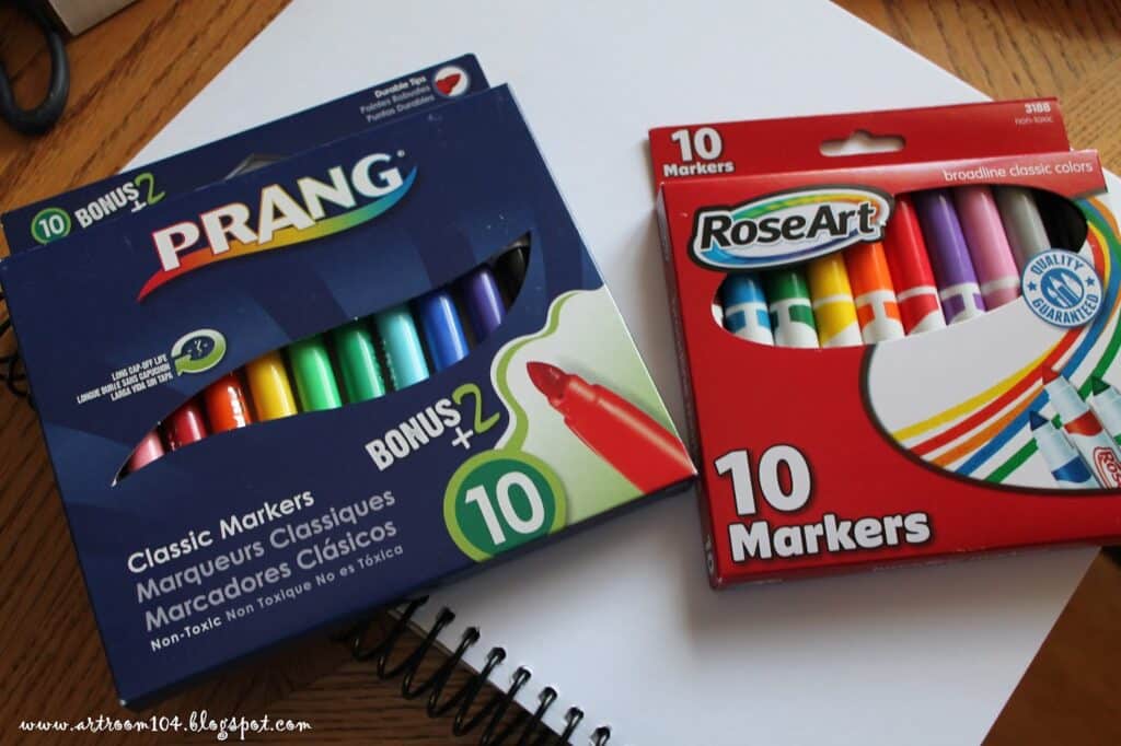 IMG_6630 Two boxes of colorful markers on a table: Prang blue box with 12 markers and RoseArt red box with 10 markers, both non-toxic. | Sky Rye Design Two boxes of colorful markers on a table: Prang blue box with 12 markers and RoseArt red box with 10 markers, both non-toxic.