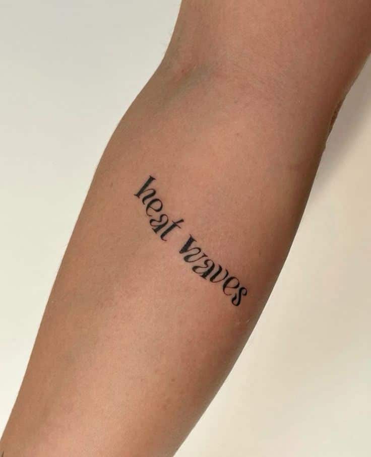 Forearm tattoo displaying the words heat waves in a stylish font, showcasing minimalist ink design on skin.