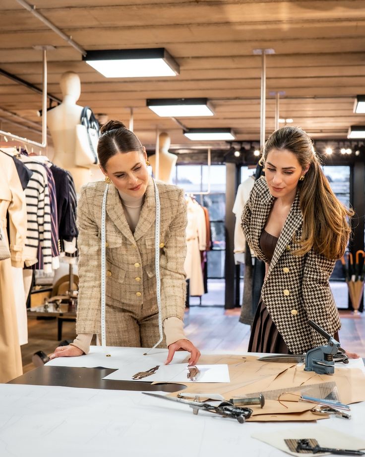Fashion designers reviewing sketches in a stylish studio, surrounded by garments and tailoring tools.