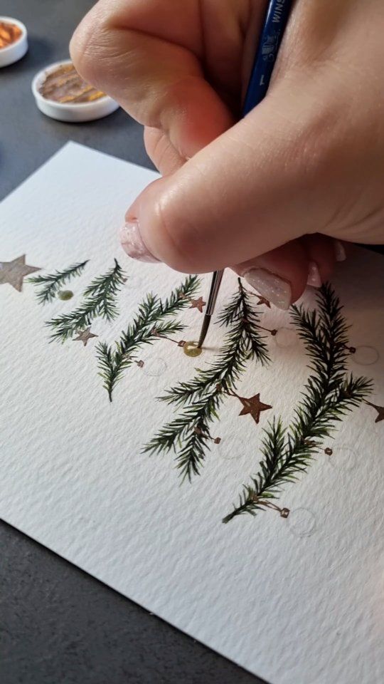 Instagram Hand painting pine branches and stars on paper with a fine brush, adding festive details for a holiday-themed art project. | Sky Rye Design Hand painting pine branches and stars on paper with a fine brush, adding festive details for a holiday-themed art project.