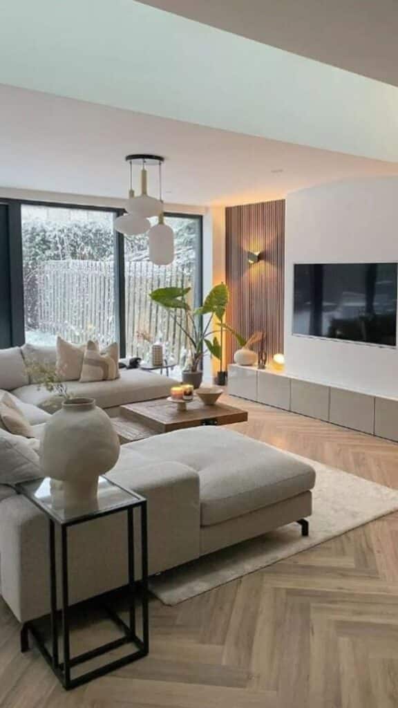 Interior design 1 Stylish modern living room with beige sofa, large TV, wooden accents, and indoor plants, overlooking a snowy garden through glass doors. | Sky Rye Design Stylish modern living room with beige sofa, large TV, wooden accents, and indoor plants, overlooking a snowy garden through glass doors.