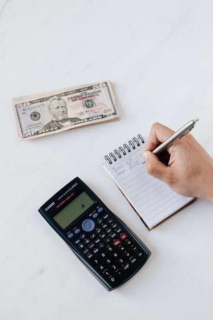 Investment in yourself Hand writing notes on a notepad with calculator and cash on desk, budgeting personal expenses and managing finances. | Sky Rye Design Hand writing notes on a notepad with calculator and cash on desk, budgeting personal expenses and managing finances.