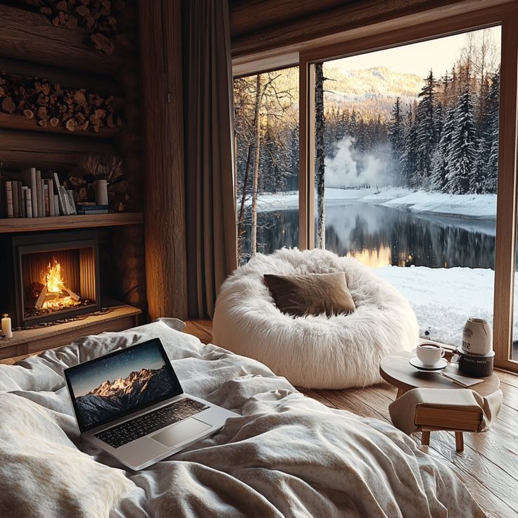 Cozy cabin interior with open laptop, fireplace, and snowy forest view by the lake, perfect for a relaxing winter retreat.