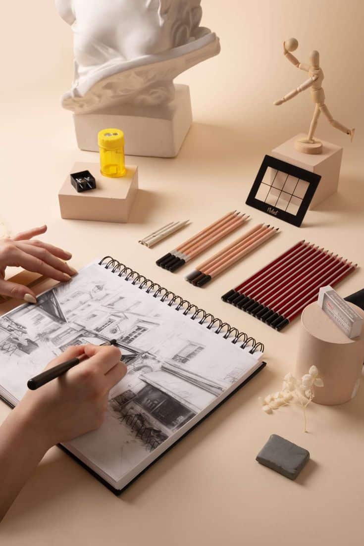 KITS DE DÉMARRAGE - Dessin - Deluxe Artist sketching architectural scene with pencils and statue, surrounded by drawing supplies on a beige background. | Sky Rye Design Artist sketching architectural scene with pencils and statue, surrounded by drawing supplies on a beige background.