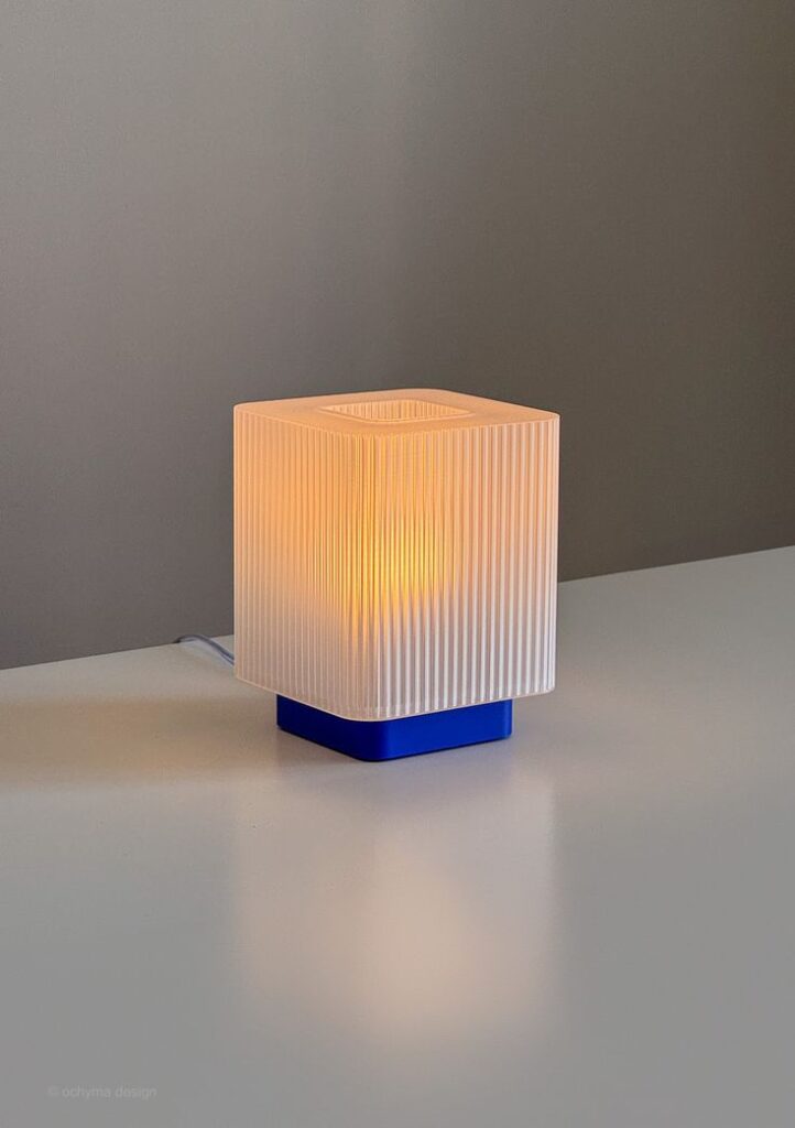 KYB - CLEAR_COBALT Modern square table lamp with ribbed shade and blue base, emitting warm light on a minimalist white surface. | Sky Rye Design Modern square table lamp with ribbed shade and blue base, emitting warm light on a minimalist white surface.