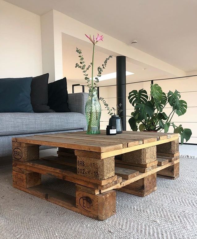 Kate Notes Interiors _ Berlin 2019 Wooden pallet coffee table with plant decor in modern living room, next to a gray sofa and lush indoor plant. | Sky Rye Design Wooden pallet coffee table with plant decor in modern living room, next to a gray sofa and lush indoor plant.