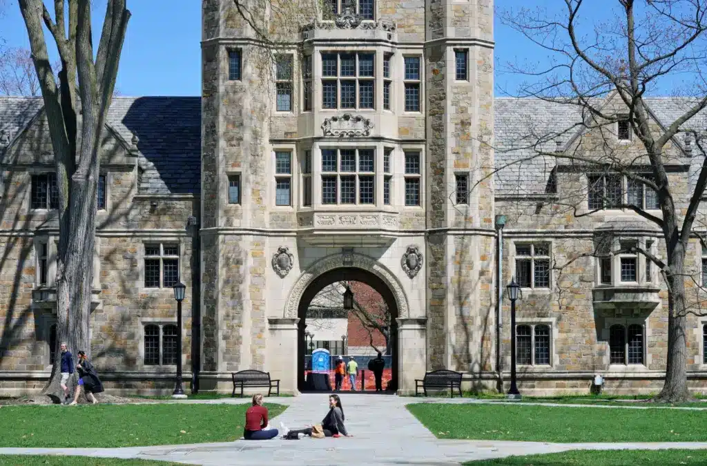 Law-School-University-of-Michigan-Ann-Arbor-Michigan Historic stone building with people relaxing on a sunny day, showcasing Gothic architecture and a peaceful campus vibe. | Sky Rye Design Historic stone building with people relaxing on a sunny day, showcasing Gothic architecture and a peaceful campus vibe.