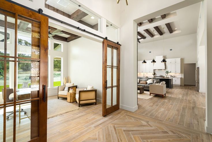 Modern open-concept living area with wooden floors, sliding glass doors, stylish furniture, and spacious kitchen under exposed beams.