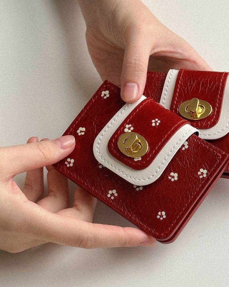 Hands holding a red floral-patterned wallet with gold clasp, featuring a stylish white trim design against a neutral background.