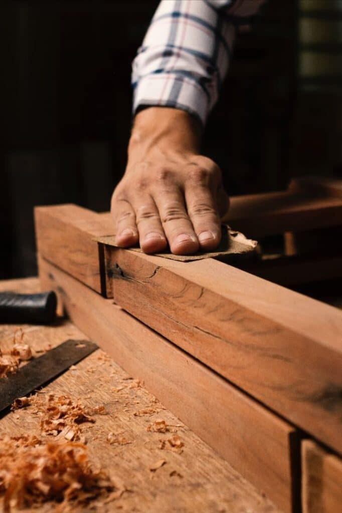 Mastering Sandpaper Grit_ Your Path to Perfect Surfaces Close-up of a hand sanding a wooden surface in a workshop, surrounded by shavings, showcasing fine woodworking craftsmanship. | Sky Rye Design Close-up of a hand sanding a wooden surface in a workshop, surrounded by shavings, showcasing fine woodworking craftsmanship.