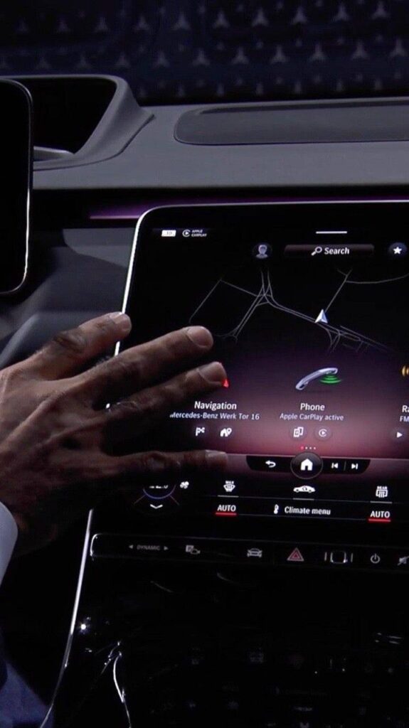 Hand interacting with car touchscreen displaying navigation and Apple CarPlay options in a luxury vehicle dashboard interface.