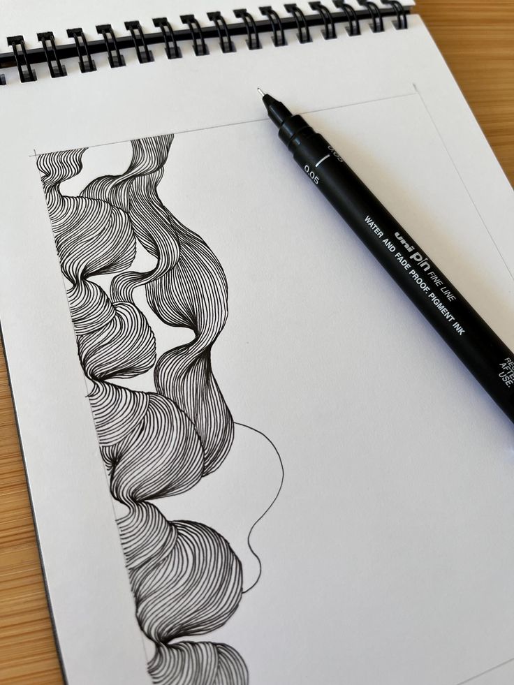Pen doodle art on sketchpad with flowing lines, created using a fine liner. Creative notebook drawing on wooden desk.