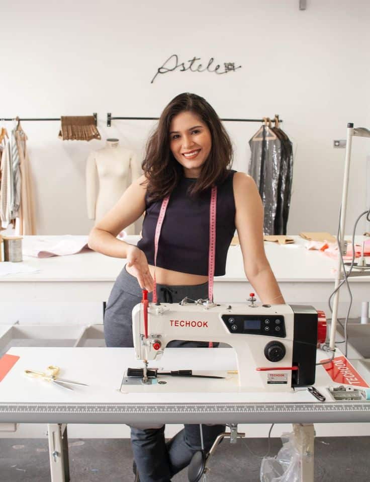 Woman smiling near sewing machine in a fashion studio, ready to create garments.