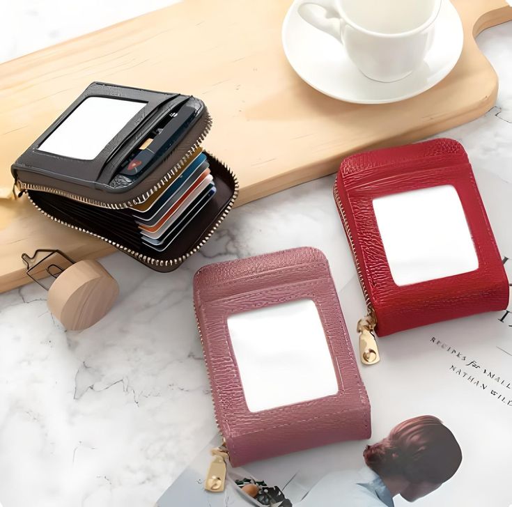 Assorted leather card holder wallets in black, pink, and red with zippers displayed on a table, featuring multiple compartments.