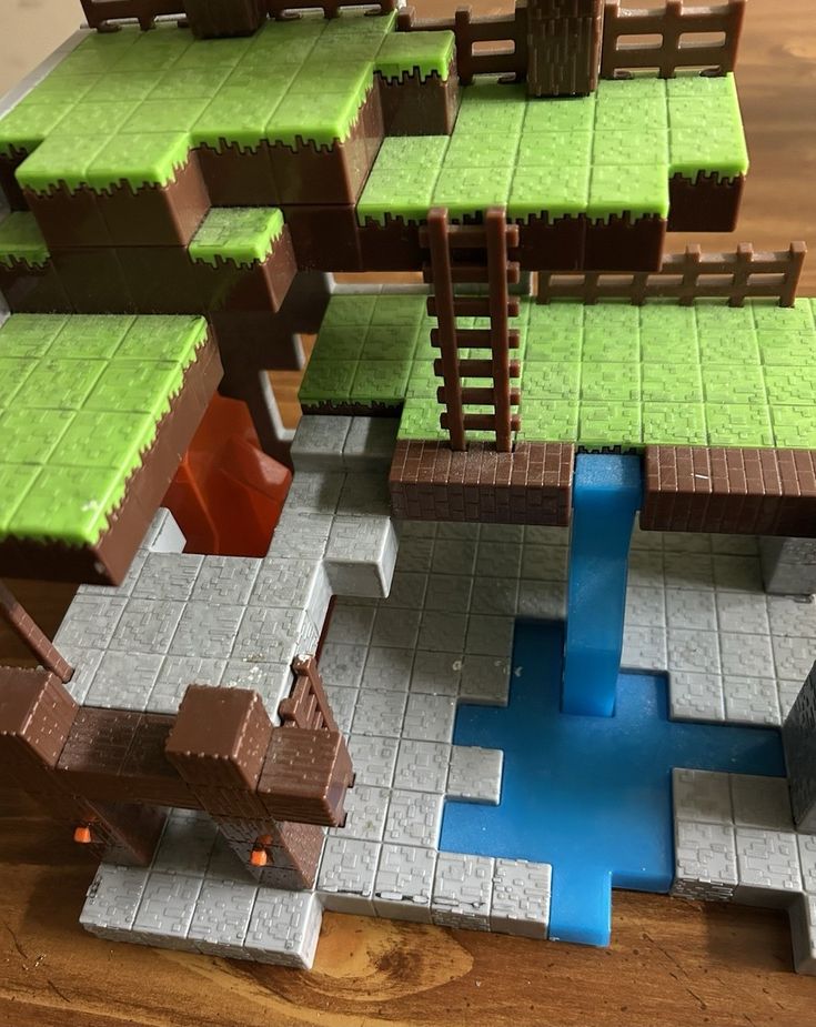 Mojang Minecraft Overworld Scene Set _ eBay Minecraft-themed block toy with grassy platforms, a wooden ladder, and blue water feature on a wooden table. | Sky Rye Design Minecraft-themed block toy with grassy platforms, a wooden ladder, and blue water feature on a wooden table.